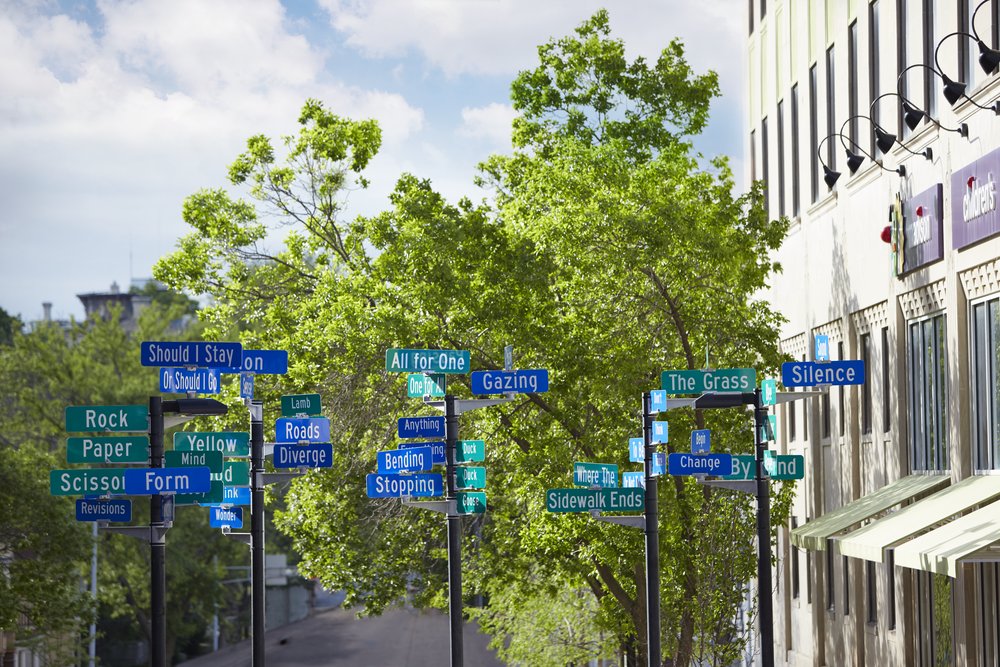 An art display of street signs labeled with playful words such as Rock, Paper, Scissors.