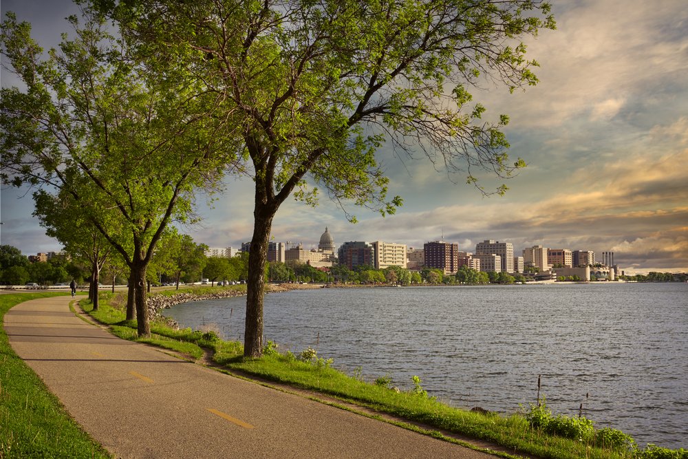 A picturesque walking trail next to a lake. The Capitol Lakes skyline can be seen in the distance.